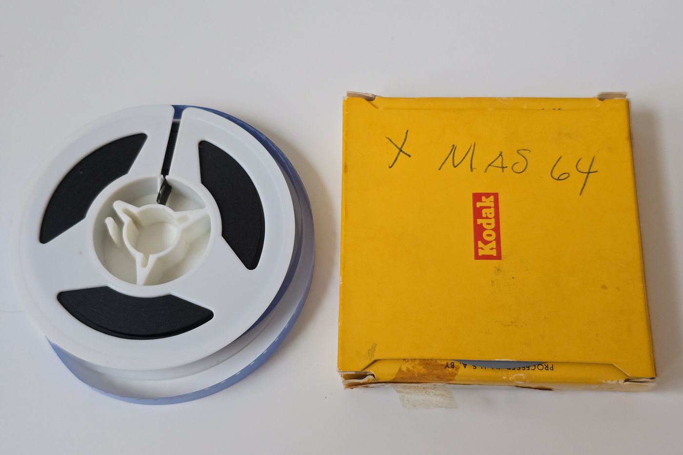 A reel of 8mm film next to its yellow Kodak box, hand-labeled X MAS 64