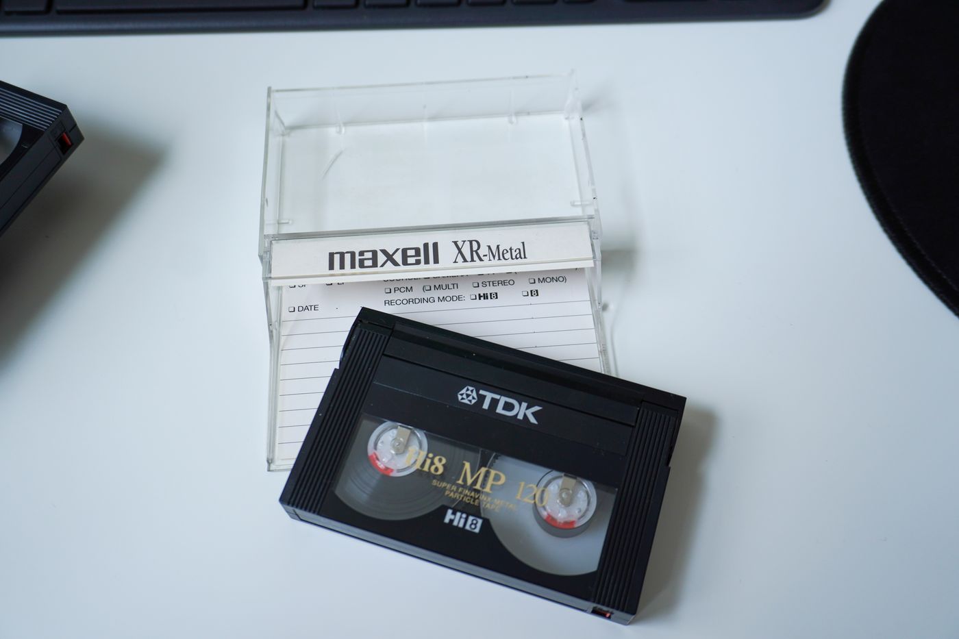 A TDK Hi8 tape in front of its clear plastic Maxell case