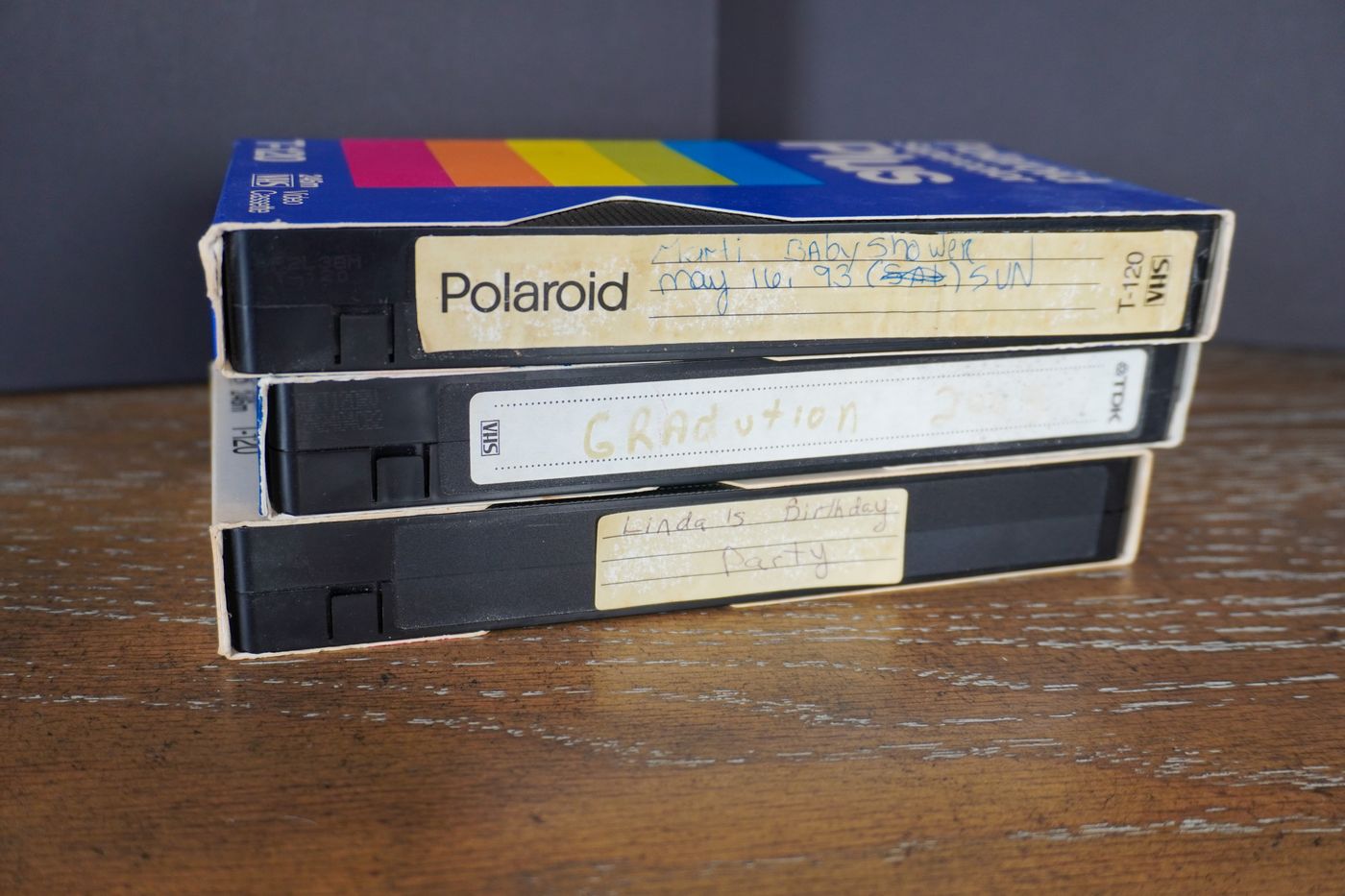 Three VHS tapes with handwritten labels stacked on a wooden table