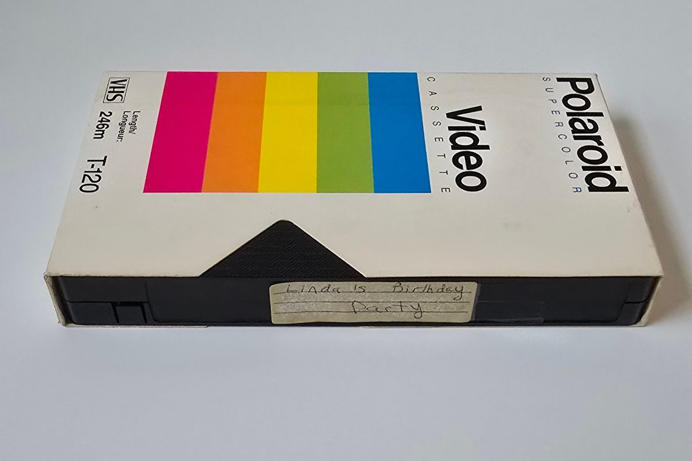 A Polaroid VHS tape in its rainbow-striped sleeve with a handwritten label reading Linda's Birthday Party